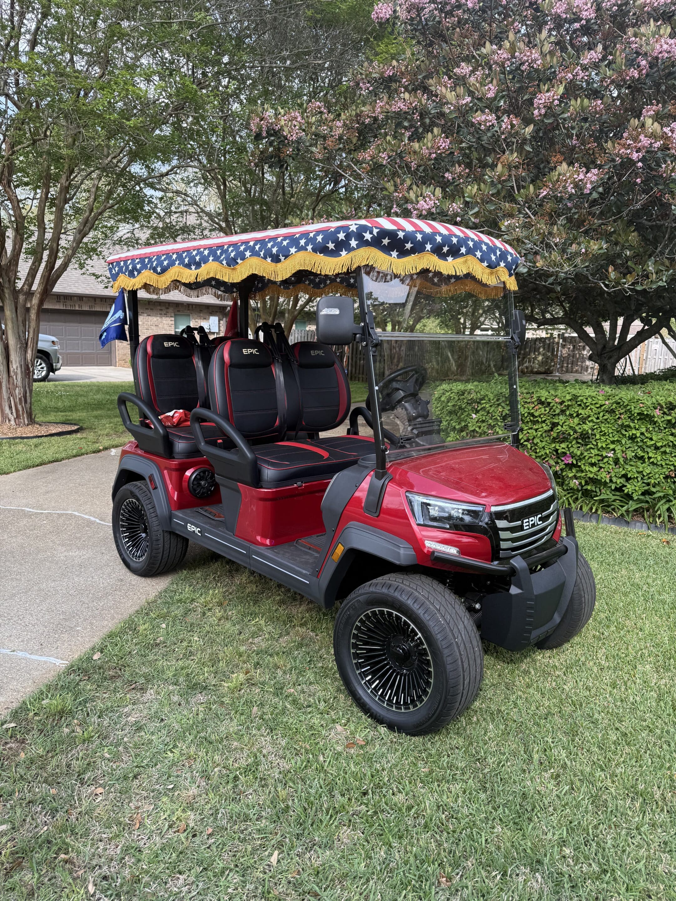 IMG_1919 Red golf cart with a star-spangled patriotic canopy and gold fringe parked on a lawn.