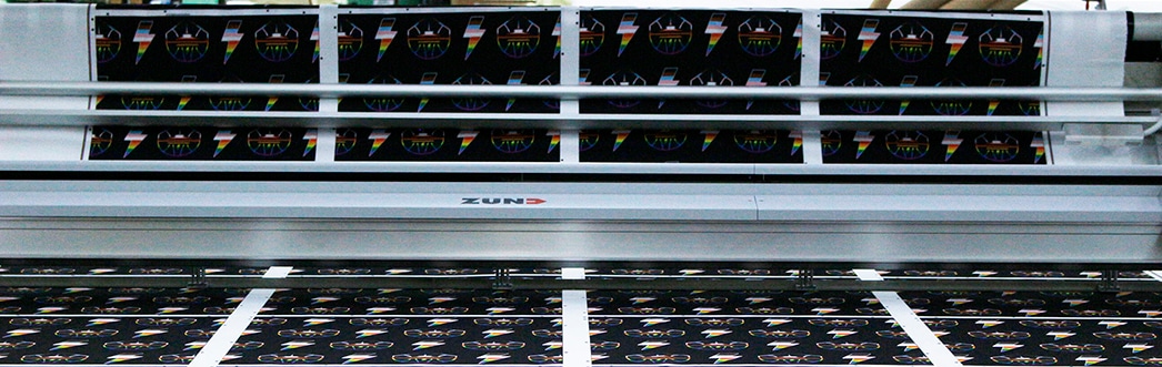 Wide-format printer feeding sheets with repeating multicolored logos; ZUND branding visible on the machine.